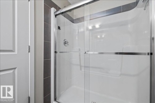 Walk-in shower featuring a chrome-framed glass enclosure, integrated shelving, and dark-toned vertical tile detailing - #31 603 Watt Bv Sw, Edmonton, AB - Indoor Photo Showing Bathroom