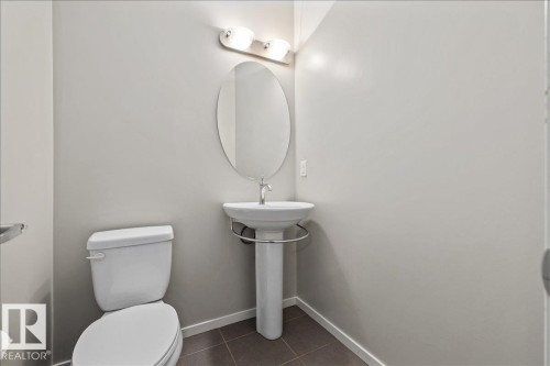 Pedestal sink with a chrome faucet, oval mirror, and wall-mounted light fixture - #31 603 Watt Bv Sw, Edmonton, AB - Indoor Photo Showing Bathroom