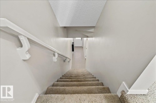 Carpeted stairway with a white wall-mounted handrail, light neutral wall paint, and white trim molding - #31 603 Watt Bv Sw, Edmonton, AB - Indoor Photo Showing Other Room