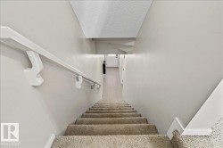Carpeted stairway with a white wall-mounted handrail, light neutral wall paint, and white trim molding - 