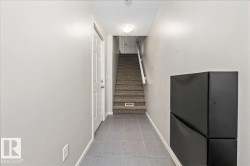 Entryway featuring light gray wall paint, gray square tile flooring, a white paneled door, and carpeted stairs with a white handrail - 