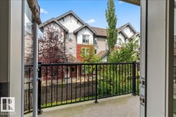 Private balcony featuring a concrete surface and black metal railings, offering views of mature trees and multi-story residential buildings with gabled roofs and varied siding - 
