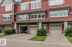 Red-sided townhome featuring multiple white-framed windows, a pitched roofline, and a private driveway leading to an attached garage - 
