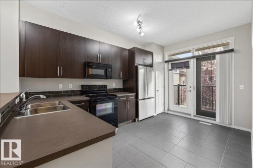 Modern kitchen with dark wood-finish cabinetry, stainless steel appliances, and a double basin sink - #31 603 Watt Bv Sw, Edmonton, AB - Indoor Photo Showing Kitchen With Double Sink