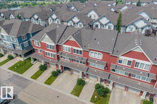 Row of townhomes featuring red and blue siding, multi-pane windows, individual attached garages, concrete driveways, and dark shingle roofs - #31 603 Watt Bv Sw, Edmonton, AB - 