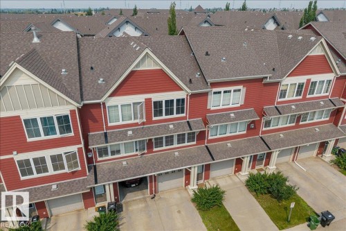 Townhome row featuring red siding with white trim, multiple windows, attached garages, and individual driveways - #31 603 Watt Bv Sw, Edmonton, AB - Outdoor With Facade