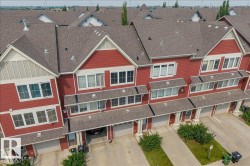 Townhome row featuring red siding with white trim, multiple windows, attached garages, and individual driveways - 
