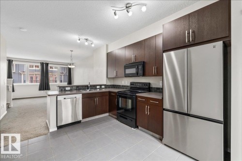 Contemporary kitchen featuring wood-finish cabinetry, stainless steel appliances, and a tiled backsplash - #31 603 Watt Bv Sw, Edmonton, AB - Indoor Photo Showing Kitchen