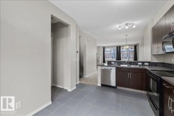 Kitchen featuring dark wood-finish cabinetry, stainless steel dishwasher, black oven, tile backsplash, and light gray tile flooring - 