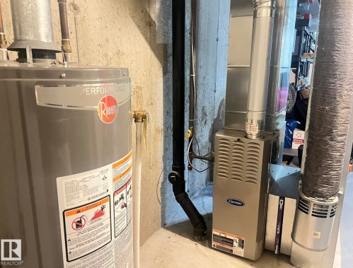 Rheem Performance water heater and Carrier furnace, featuring a power vent system and ductwork, set against a concrete wall - 5001 62 Street, Beaumont, AB 