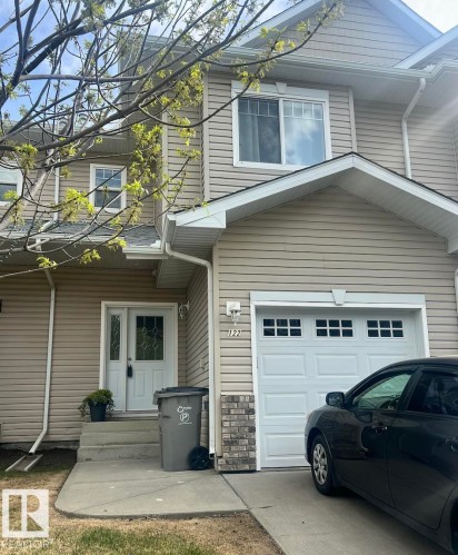 Two-story residential exterior featuring light-colored horizontal siding and a white paneled garage door with upper window inserts - 5001 62 Street, Beaumont, AB 