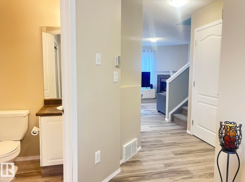 Powder room featuring a toilet, a vanity with a white cabinet, and a mirror - 5001 62 Street, Beaumont, AB 