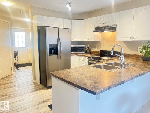 Kitchen featuring white cabinetry, stainless steel appliances, a double basin sink with a high-arc faucet, and wood-finish flooring - 5001 62 Street, Beaumont, AB 