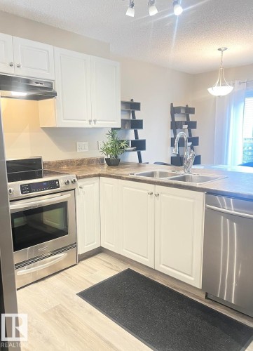 Kitchen featuring white cabinetry, light wood-finish flooring, stainless steel appliances, a double basin sink, and laminate countertops - 5001 62 Street, Beaumont, AB 