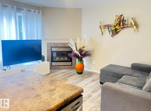 Living area featuring light wood-finish flooring, a corner fireplace with tile surround and mantel, and neutral wall paint - 5001 62 Street, Beaumont, AB 