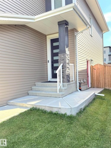 Front entry featuring a contemporary door, stone-clad pillar, and white railing - 20827 130 Avenue Nw, Edmonton, AB 