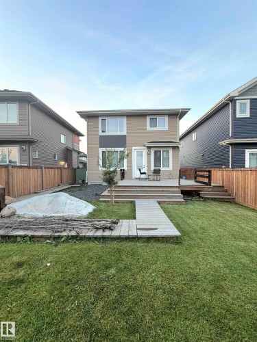 Two-story exterior with light beige siding and white trim, featuring a multi-level wood deck, wood privacy fencing, and a grassy yard - 20827 130 Avenue Nw, Edmonton, AB 