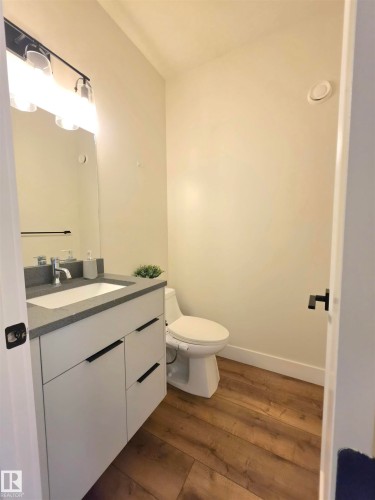 White vanity with dark gray countertop, undermount sink, and wood-finish flooring - 20827 130 Avenue Nw, Edmonton, AB 