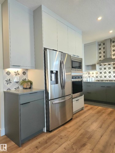 Stainless steel refrigerator, built-in microwave, wood-finish flooring, two-tone cabinetry, and patterned tile backsplash - 20827 130 Avenue Nw, Edmonton, AB 