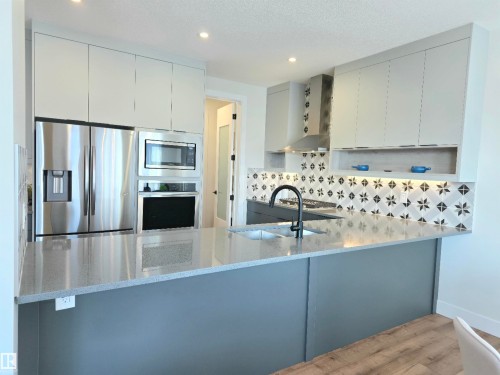 Contemporary kitchen featuring white cabinetry with stainless steel appliances, including a French-door refrigerator, dual wall ovens, and microwave - 20827 130 Avenue Nw, Edmonton, AB 