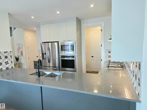 Kitchen island with a double basin sink and matte black faucet, stainless steel appliances, built-in wall oven, and gas cooktop - 20827 130 Avenue Nw, Edmonton, AB 
