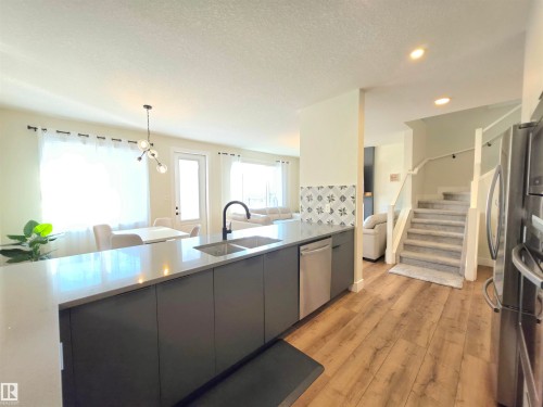 Kitchen island with a light-toned countertop, integrated stainless steel dishwasher, and a matte black faucet - 20827 130 Avenue Nw, Edmonton, AB 
