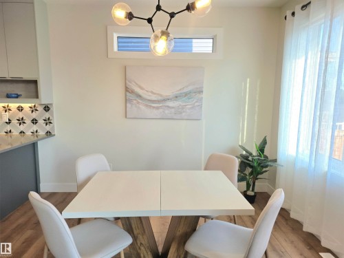 Modern dining space featuring a light wood extendable table, four upholstered chairs with neutral fabric, and warm ambient lighting from a contemporary three-globe pendant fixture - 20827 130 Avenue Nw, Edmonton, AB 