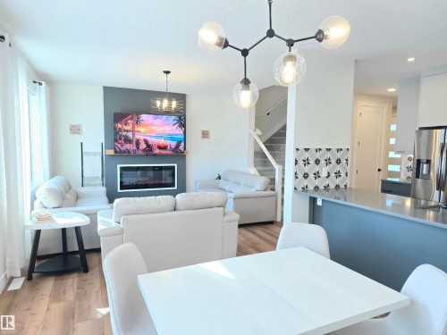 Open-concept living space with wood-finish flooring, a contemporary fireplace, and a kitchen island with a smooth countertop - 20827 130 Avenue Nw, Edmonton, AB 