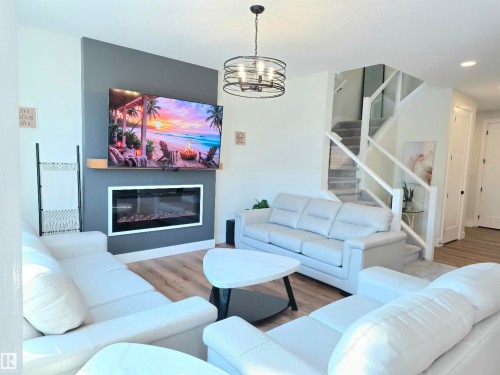 Integrated electric fireplace with a wood mantle, wood-finish flooring, and a modern stair railing with glass panels - 20827 130 Avenue Nw, Edmonton, AB 