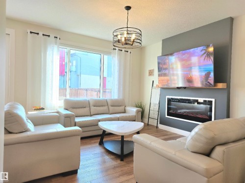 Recessed electric fireplace with a floating wood mantle, wood-finish flooring, and a contemporary ceiling light fixture - 20827 130 Avenue Nw, Edmonton, AB 