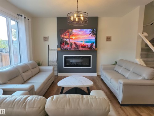 Living space featuring wood-finish flooring, a contemporary electric fireplace with a white surround, and a dark accent wall - 20827 130 Avenue Nw, Edmonton, AB 