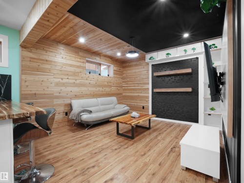 Wood-finish flooring throughout, featuring a horizontal wood-paneled wall, black ceiling with recessed lighting, and a built-in shelving unit - 20827 130 Avenue Nw, Edmonton, AB 