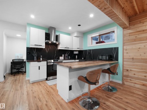Kitchen featuring white cabinetry, black stone-look backsplash, wood-finish flooring, and a natural wood ceiling - 20827 130 Avenue Nw, Edmonton, AB 