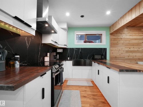 Modern kitchen featuring white cabinetry, wood-finish countertops, black patterned backsplash, and an undermount stainless steel sink - 20827 130 Avenue Nw, Edmonton, AB 