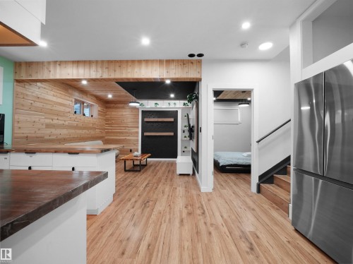 Wood-finish flooring throughout, stainless steel refrigerator, white cabinetry with wood-finish countertops, recessed lighting, and wood paneling - 20827 130 Avenue Nw, Edmonton, AB 