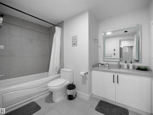 Bathtub with subway tile surround, white toilet, single vanity with a solid surface countertop, white cabinetry with black hardware, and an illuminated mirrored medicine cabinet - 20827 130 Avenue Nw, Edmonton, AB 
