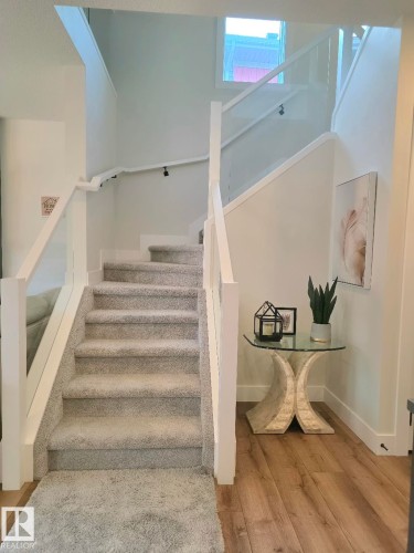 Carpeted staircase with glass panel railings, white risers, and wood-finish flooring at the base - 20827 130 Avenue Nw, Edmonton, AB 