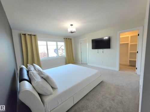Plush gray carpeting throughout, featuring large windows with white trim, a modern ceiling light fixture, and an open doorway to a walk-in closet with built-in shelving - 20827 130 Avenue Nw, Edmonton, AB 