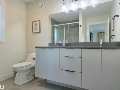 Dual vanity with dark stone countertop, undermount sinks, and light-colored cabinetry with modern hardware - 20827 130 Avenue Nw, Edmonton, AB 