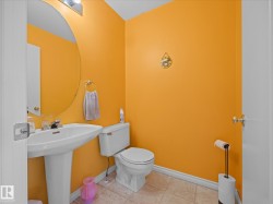 Pedestal sink with chrome-finish faucet, circular wall mirror, and overhead vanity lighting in a powder room - 