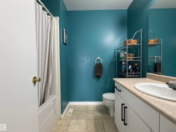 Spa-inspired bathroom featuring teal-painted walls, ceramic tile flooring, a white vanity with black hardware and a rounded vessel sink, toilet, and a framed mirror with integrated shelving - 
