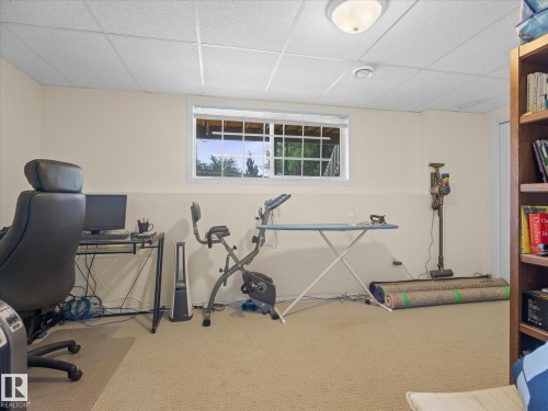 Carpeted room featuring a white drop ceiling, single window with exterior tree views, and built-in shelving - #15 11717 9B Av Nw, Edmonton, AB - Indoor