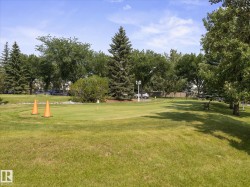 Expansive green space featuring a putting green, mature trees, manicured landscaping, and a park bench - 
