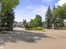 Gated community entrance featuring stone pillars, mature evergreen trees, and manicured landscaping - 