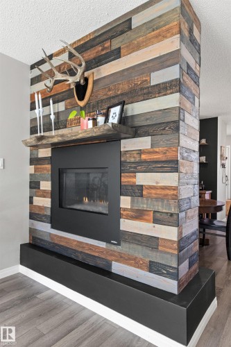 Freestanding fireplace with a wood plank façade, featuring a built-in firebox, a substantial wood mantel, and a dark base - 4306 Prowse Link Link Sw, Edmonton, AB 