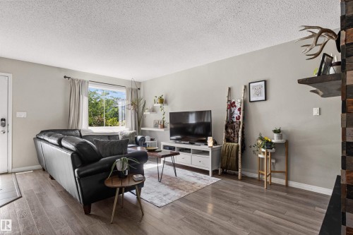 Wood-finish flooring, light grey wall paint, a window with exterior tree views, and built-in white floating shelves - 4306 Prowse Link Link Sw, Edmonton, AB 