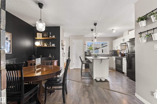 Wood-finish flooring throughout, white kitchen cabinetry, black appliances, and a kitchen island with seating - 4306 Prowse Link Link Sw, Edmonton, AB 