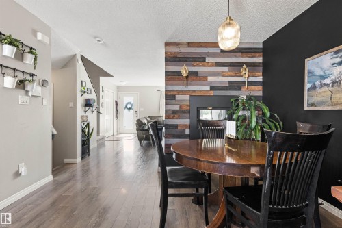 Modern decorative fireplace with a wood panel accent wall, wood-finish flooring, and a contemporary pendant light fixture - 4306 Prowse Link Link Sw, Edmonton, AB 