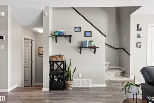 Wood-finish flooring, light gray wall paint, white trim, carpeted staircase with dark handrails, and a hallway with a flush-mount light - 4306 Prowse Link Link Sw, Edmonton, AB 