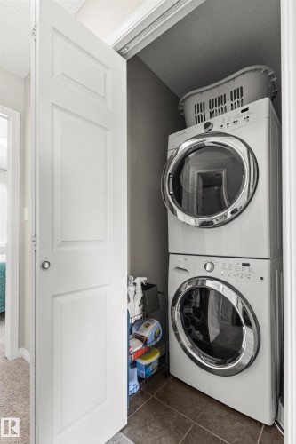 Dedicated laundry area featuring a stacked washer and dryer, tiled flooring, and a solid white door - 4306 Prowse Link Link Sw, Edmonton, AB 